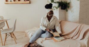 brown-skinned woman with kinky hair sits on a light tan couch reading