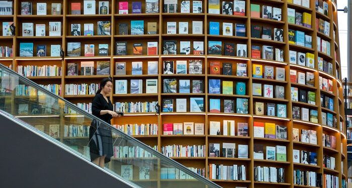 person going down an escalator with giant bookshelves in the background spanning both floors