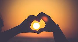 a photograph of a person's hands making the shape of a heart, silhouetted against a sunset