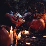 hands holding an animal skull in a dark space filled with candles and pumpkins