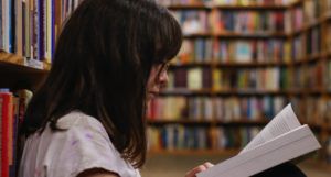 a photo of a girl reading sitting on the floor of a library